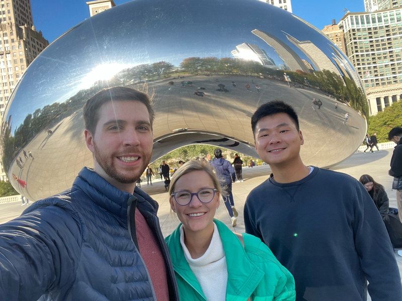 Three people stand in front of Chicago’s Cloud Gate sculpture, also known as “The Bean.”